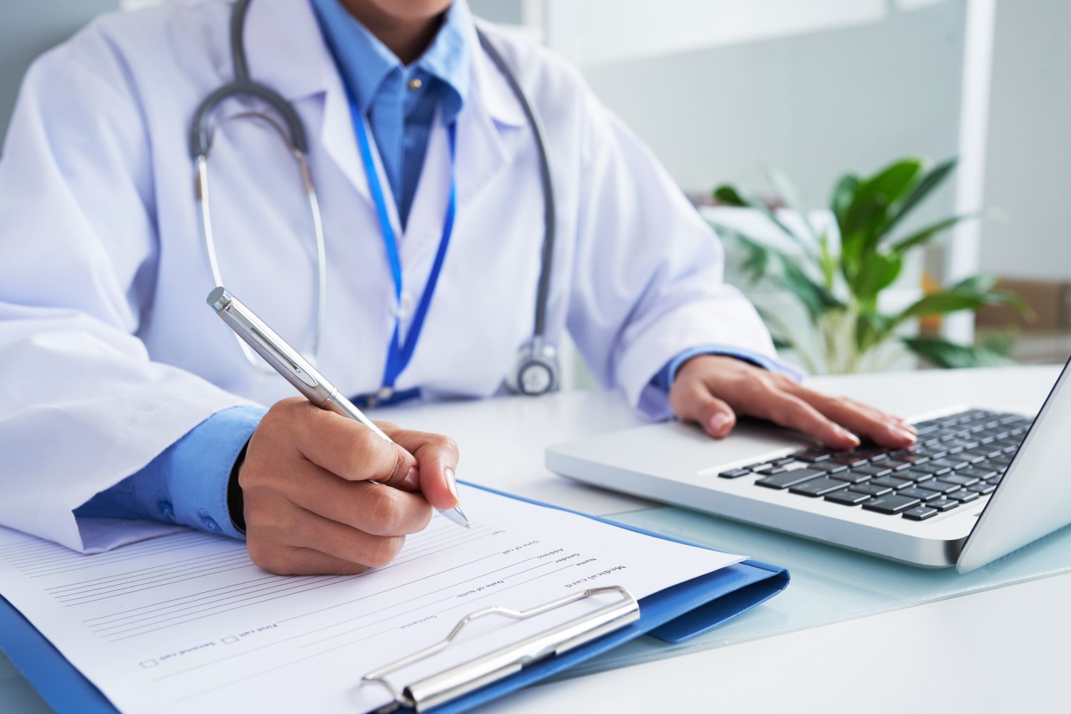 Profissional de saúde preenchendo ficha médica ao lado de um notebook